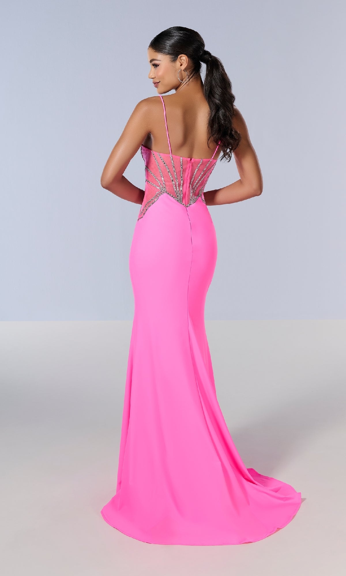 A woman stands facing away against a plain light background, wearing the Tiffany 16201 long prom dress in bright pink, featuring a slim fit and rhinestone-embellished sheer panels on the back.